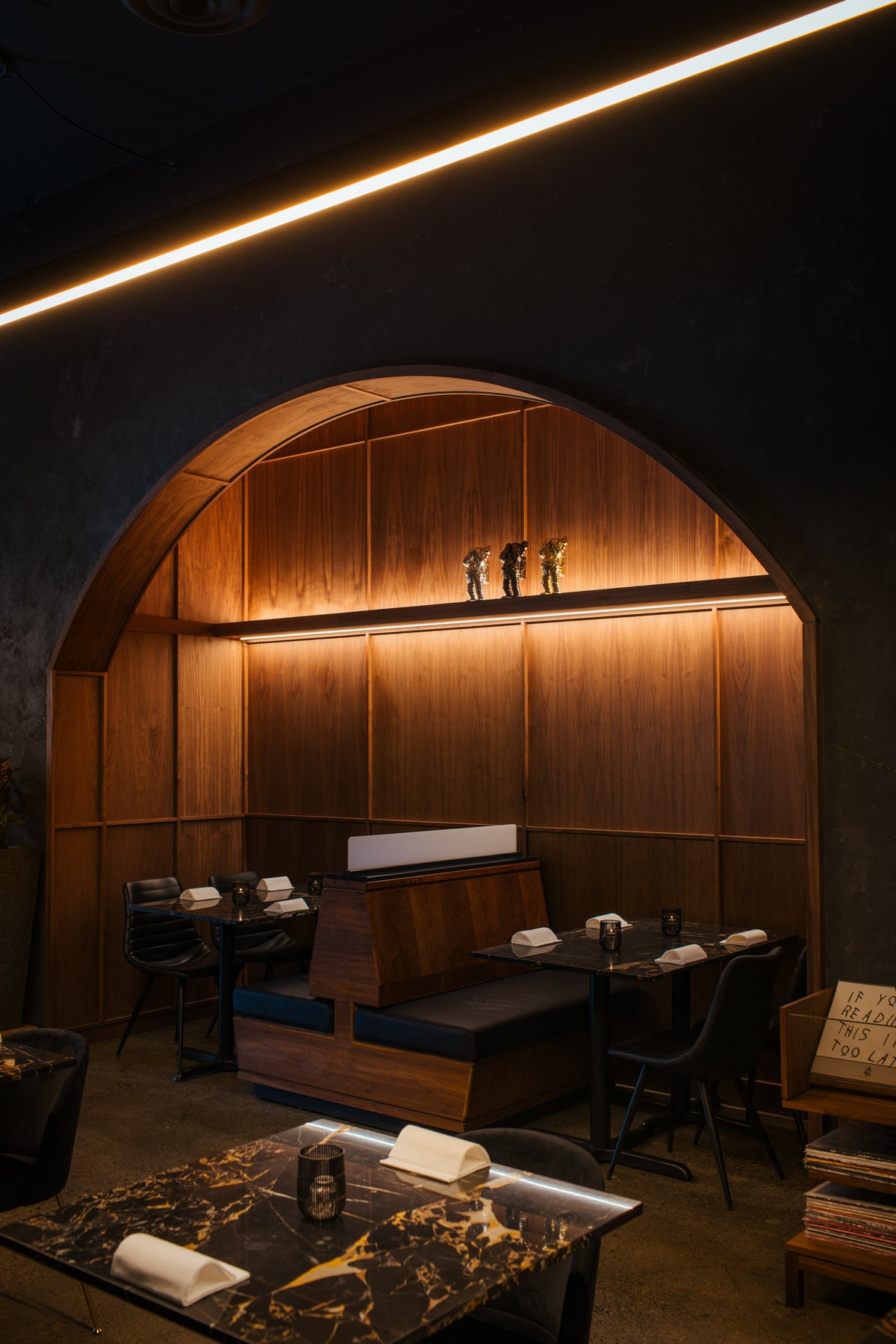 Recessed LED lighting within a floating walnut shelf illuminating display elements and table seating inside the AnnaLena dining alcove.