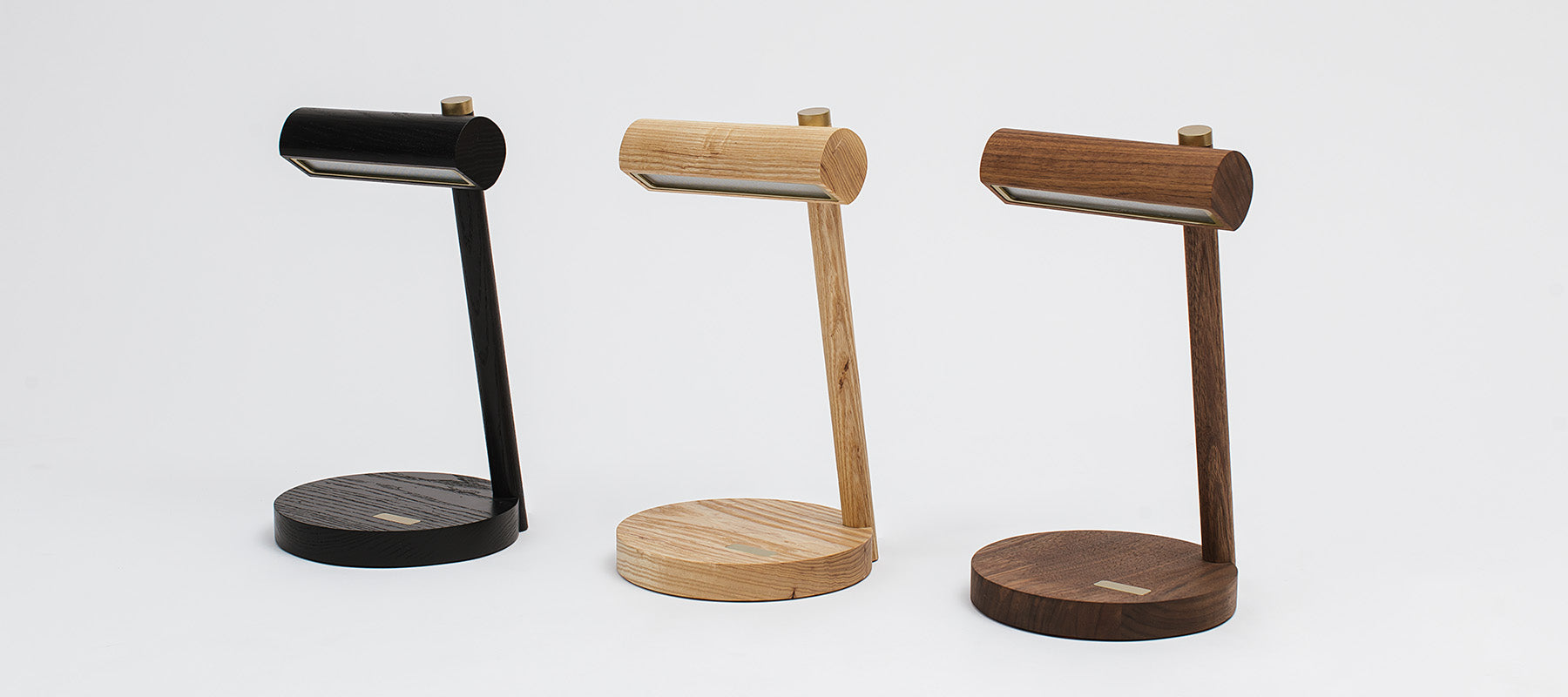 Three versions of the touch n go table lamp, Natural Ash, Black Ash and Walnut. Minimal in aesthetic, the lamps feature brass accents and a touch pad for on/off and dimming