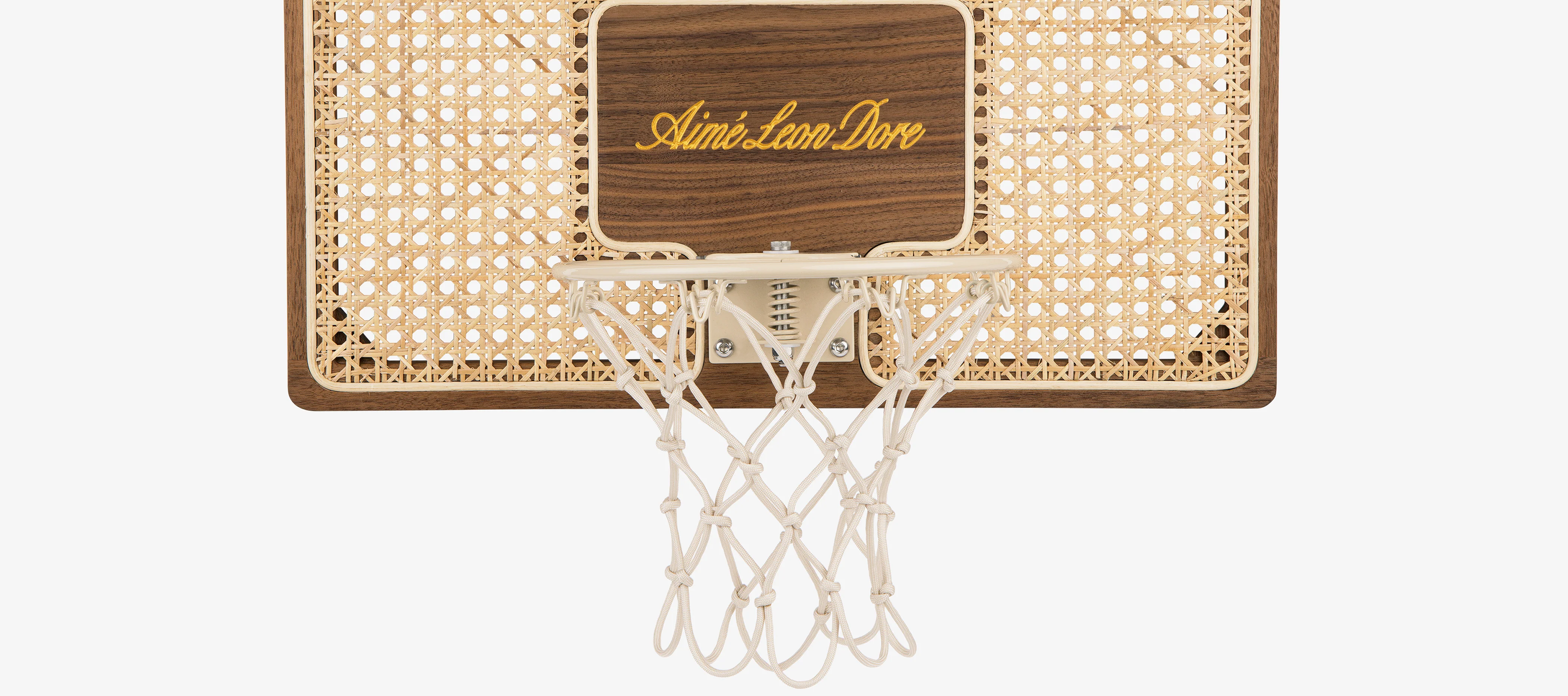 Close-up detail of solid walnut frame and hand-woven rattan panel on Aimé Leon Dore collaboration mini basketball hoop.